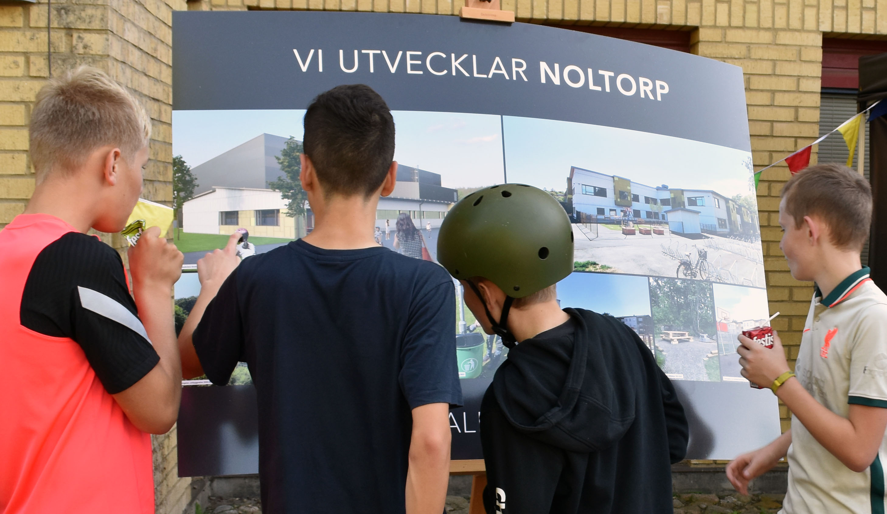 Fyra barn med skolväskor står framför en poster med texten "Vi utvecklar Noltorp"